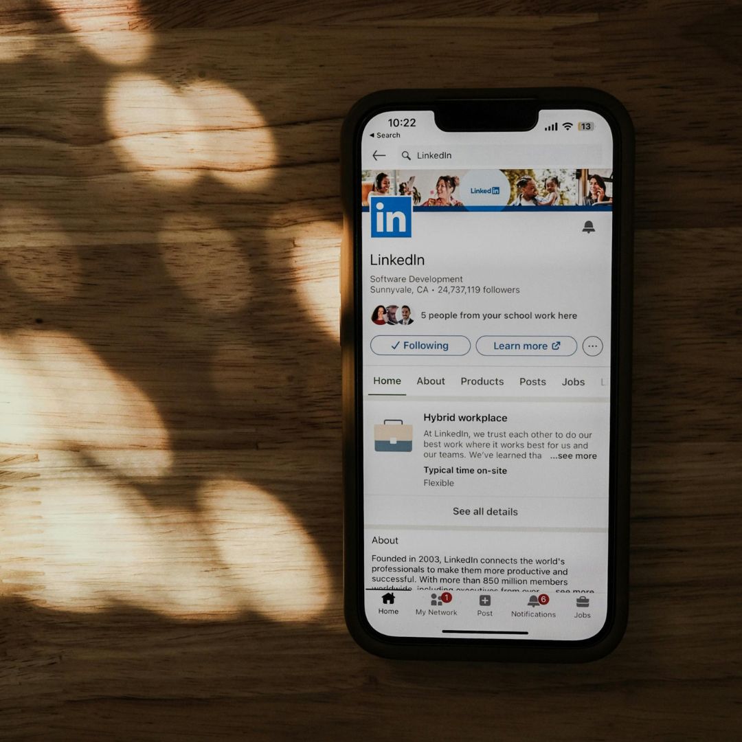 LinkedIn content framework. A smartphone displays the LinkedIn profile page on a wooden surface, with soft, dappled sunlight creating patterns. The atmosphere is calm and professional.